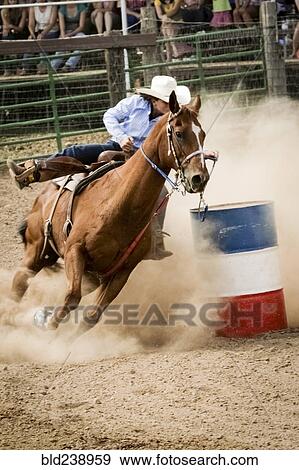 Stock Photo - Cowgirl riding horse near barrel in rodeo. Fotosearch