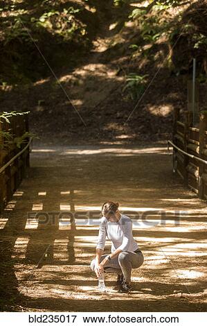 Crouching woman holding water bottle on sunny path View Large Photo Image Stock Photo - Crouching woman holding water bottle on sunny path. Fotosearch