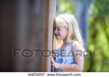 Stock Photo - Curious Caucasian girl peeking through wooden fence. Fotosearch