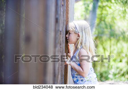 Stock Photo - Curious Caucasian girl peeking through wooden fence. Fotosearch