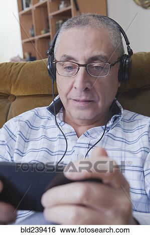 Stock Photograph - Curious Hispanic man listening to cell phone with headphones. Fotosearch