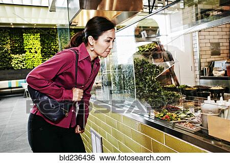 Stock Photograph - Curious Japanese businesswoman looking at salad in food court. Fotosearch