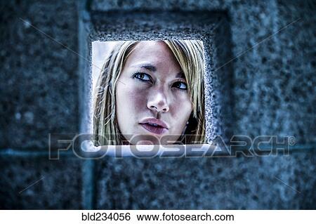 Stock Photograph - Curious Mixed Race woman looking through stone wall. Fotosearch