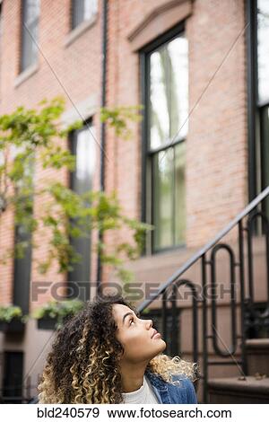 Curious Mixed Race woman looking up in city View Large Photo Image Stock Photo - Curious Mixed Race woman looking up in city. Fotosearch