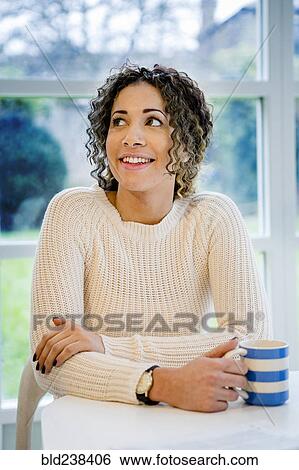Curious woman sitting at table holding coffee cup View Large Photo Image Stock Photograph - Curious woman sitting at table holding coffee cup. Fotosearch