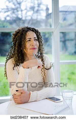 Curious woman sitting at table with pen and notepad View Large Photo Image Stock Photo - Curious woman sitting at table with pen and notepad. Fotosearch