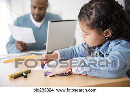 Picture - Daughter coloring with crayons while father uses laptop. Fotosearch