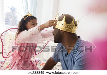 Stock Photo - Daughter wearing costume placing crown on father. Fotosearch