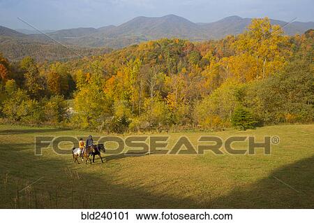 Stock Image - Distant Caucasian couple horseback riding in field. Fotosearch