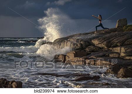 Picture - Distant Caucasian woman doing yoga on rocks near ocean. Fotosearch