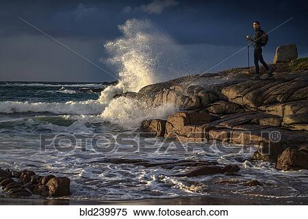 Stock Photography - Distant Caucasian woman hiking on rocks near ocean. Fotosearch