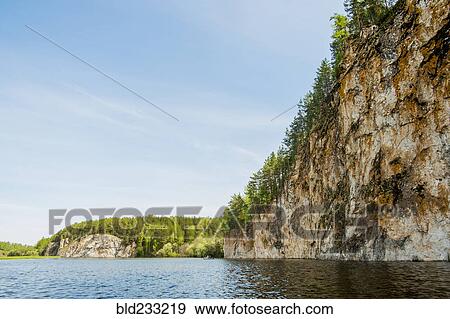 Stock Photo - Distant inflatable raft on river near cliff. Fotosearch