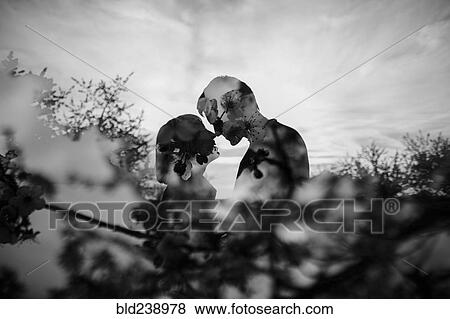 Stock Photo - Double exposure of Caucasian couple kissing near trees. Fotosearch
