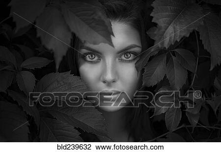 Stock Image - Face of Caucasian woman behind foliage. Fotosearch