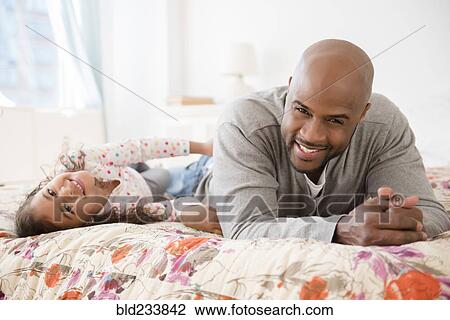 Stock Image - Father and daughter laying on bed. Fotosearch