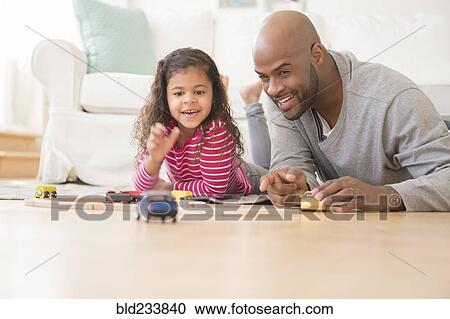 Stock Image - Father and daughter playing with toy cars on floor. Fotosearch
