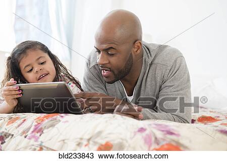 Stock Image - Father and daughter using digital tablet on bed. Fotosearch