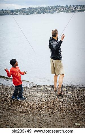 Stock Photo - Father and son throwing rocks into river. Fotosearch