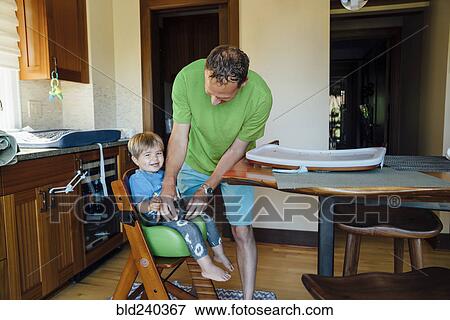 Stock Photo - Father buckling son into highchair. Fotosearch