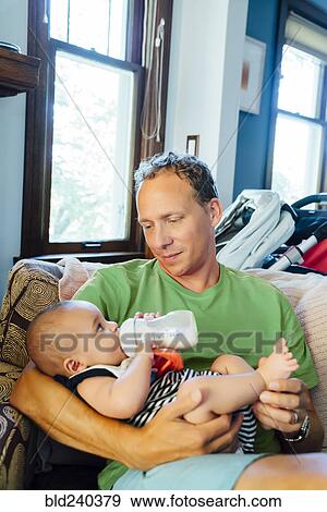 Stock Photo - Father holding baby son drinking milk from bottle. Fotosearch