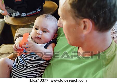 Stock Photo - Father holding baby son playing with toy. Fotosearch