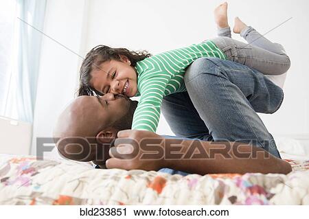Stock Image - Father kissing daughter on bed. Fotosearch