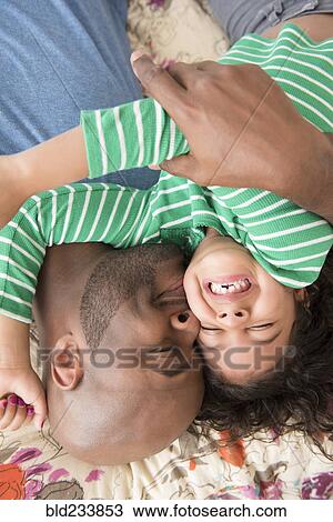 Stock Image - Father kissing daughter on bed. Fotosearch