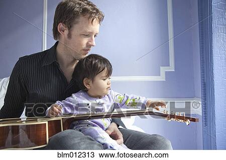 Stock Image - Father sitting with baby girl and guitar. Fotosearch