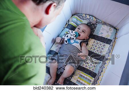 Stock Image - Father watching baby son in crib. Fotosearch