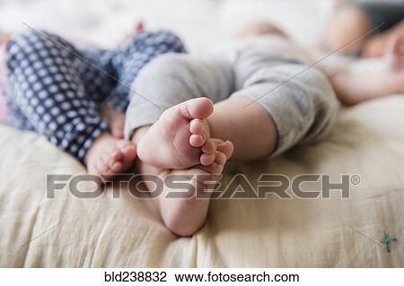 Stock Image - Feet of Caucasian twin baby girls laying on bed. Fotosearch