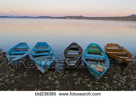 Five empty rowboats on rocky shore of lake at sunset View Large Photo Image Stock Photography - Five empty rowboats on rocky shore of lake at sunset. Fotosearch