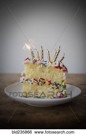Stock Photograph - Flickering candle burning cake with sprinkles on plate. Fotosearch