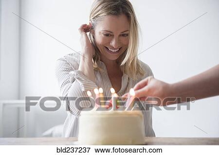 Stock Photo - Friend lighting candles on birthday cake for Caucasian woman . Fotosearch