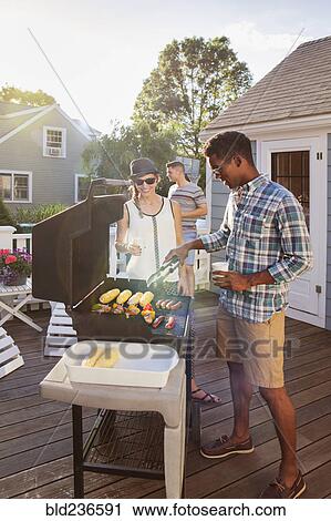 Friends cooking food on grille at barbecue on patio View Large Photo Image Stock Image - Friends cooking food on grille at barbecue on patio. Fotosearch