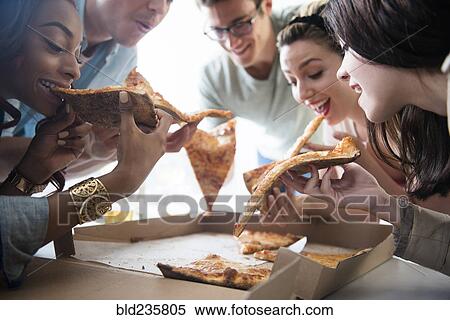 Stock Photography - Friends eating slices of pizza. Fotosearch