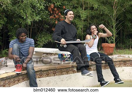 Stock Image - Friends hanging out at edge of disused swimming pool. Fotosearch