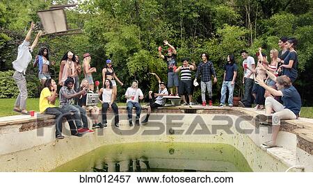 Stock Photo - Friends hanging out at edge of disused swimming pool. Fotosearch