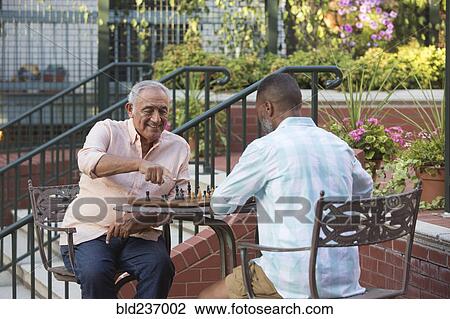 Stock Image - Friends playing chess in garden. Fotosearch