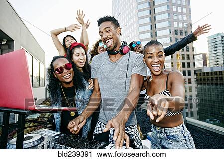 Stock Image - Friends posing with DJ on urban rooftop. Fotosearch