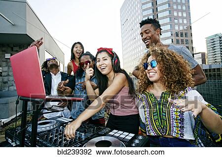 Stock Image - Friends posing with DJ on urban rooftop. Fotosearch