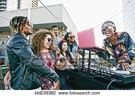 Stock Image - Friends smiling with DJ on urban rooftop. Fotosearch