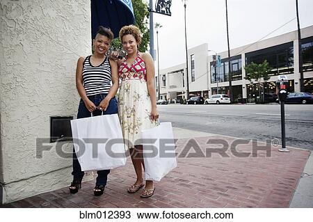 Stock Image - Friends standing on city sidewalk holding shopping bags. Fotosearch