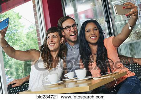 Friends taking cell phone selfie in coffee shop View Large Photo Image Stock Image - Friends taking cell phone selfie in coffee shop. Fotosearch