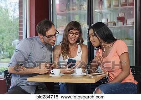 Friends texting on cell phone in coffee shop View Large Photo Image Stock Photography - Friends texting on cell phone in coffee shop. Fotosearch