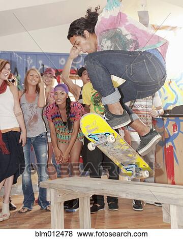 Stock Photo - Friends watching man on skateboard at party. Fotosearch