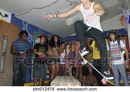 Stock Photo - Friends watching man on skateboard at party. Fotosearch
