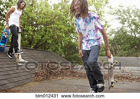 Stock Image - Friends with skateboards hanging out on roof. Fotosearch