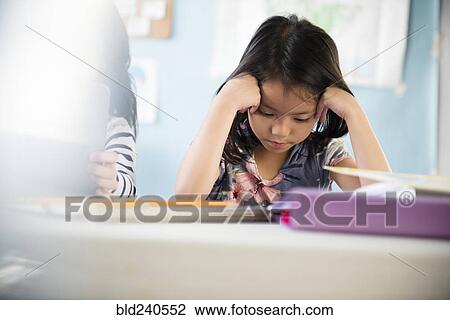 Stock Image - Frustrated girl with head in hands in classroom. Fotosearch