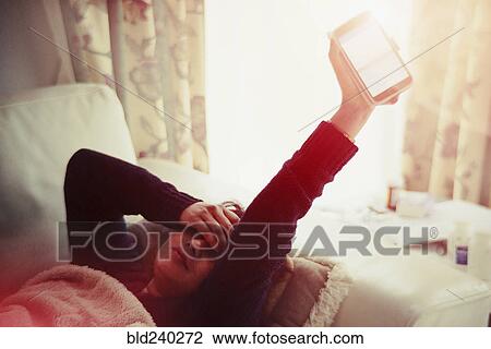 Stock Image - Frustrated Indian woman laying on sofa holding glowing cell phone. Fotosearch