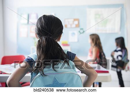 Stock Photo - Girl in classroom wearing backpack watching classmates. Fotosearch